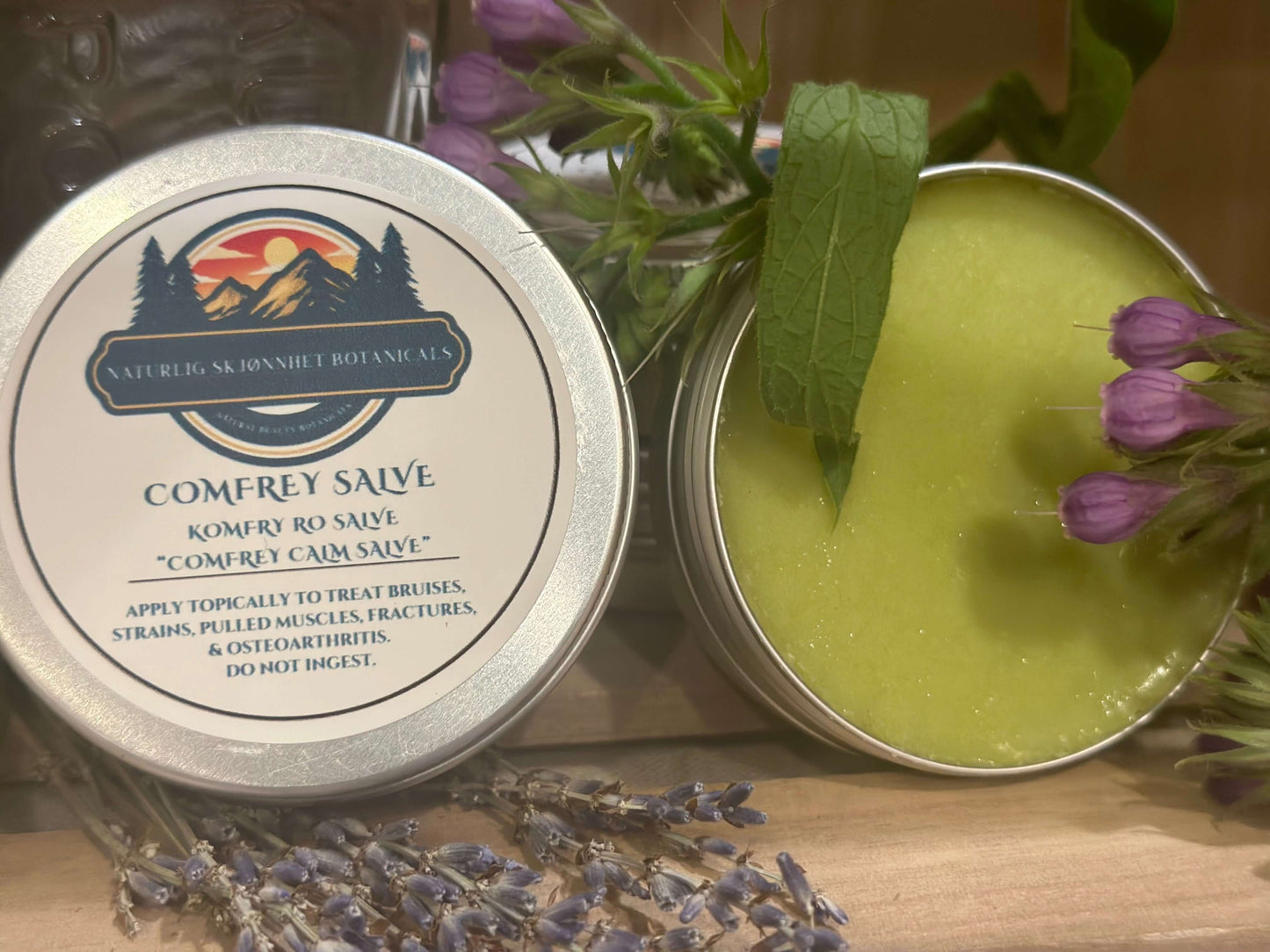 Comfrey salve in tin with label and lavender, showcasing natural ingredients for skin and joint relief.