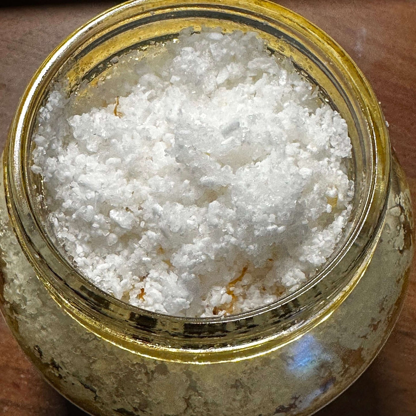 Close-up of a jar filled with white sea salt and botanicals for a natural body scrub.
