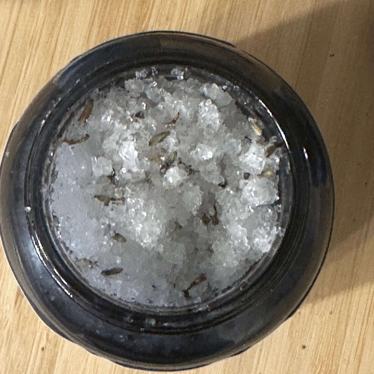 Close-up of a jar filled with natural body scrub containing sea salt and botanical ingredients.