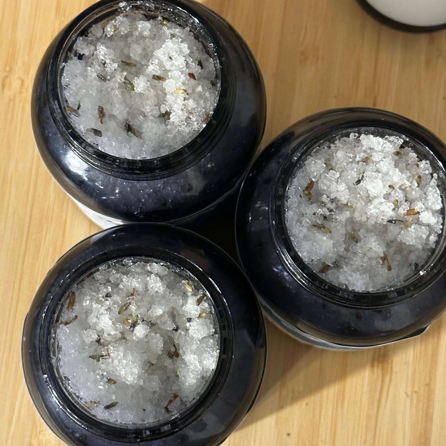 Three jars of botanical body scrub featuring Epsom and sea salt, designed for smooth and glowing skin.