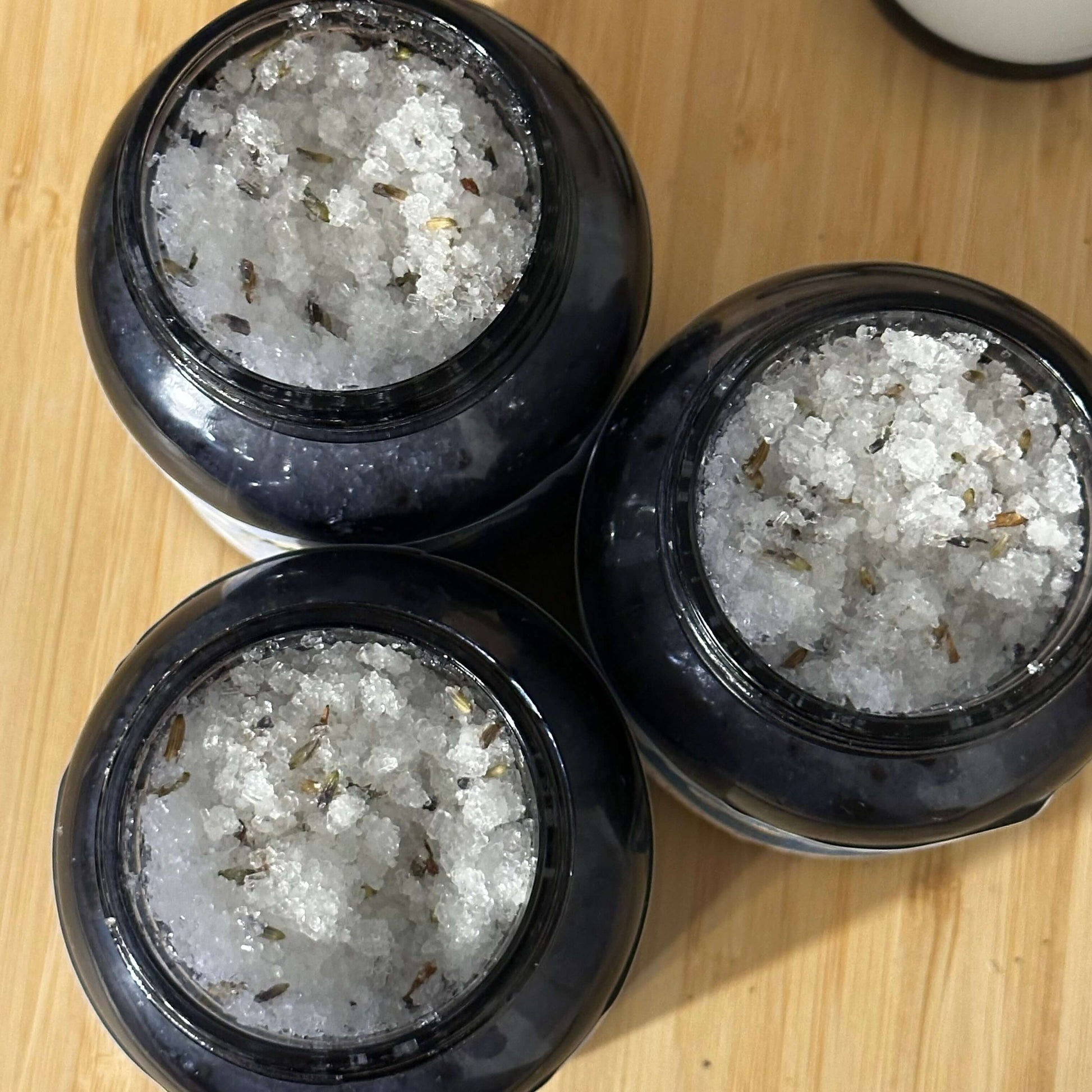 Three jars of botanical body scrub featuring Epsom and sea salt, designed for smooth and glowing skin.
